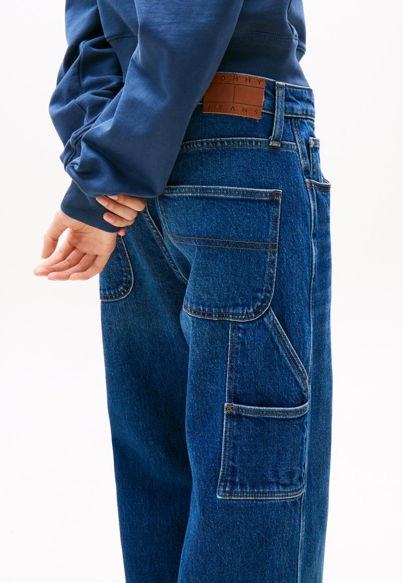Blaue Denim-Cargo-Hosen mit mehreren Taschen, geradem Schnitt und Kontrastnähten. Begleitet von einem marineblauen Sweatshirt.
