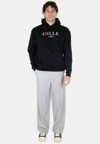 Felpa nera con tasca frontale, testo del logo bianco. Abbinata a pantaloni larghi grigi chiari e sneakers nere con suola bianca.