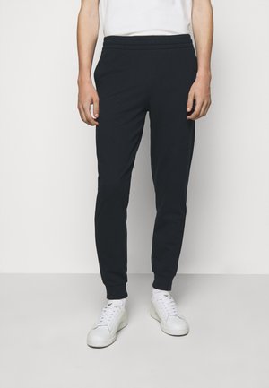 Pantaloni joggers blu realizzati in tessuto morbido, con vita a coste, gambe affusolate e polsini elasticizzati, abbinati a sneakers bianche.