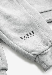 Sive trenirke z ribastim manžetami, gladko teksturo in natisnjenim logotipom "BAKER by Ted Baker" v črni barvi na predelu stegna.