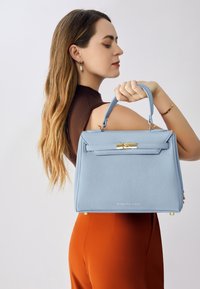 Sac à main structuré bleu clair en cuir texturé, avec un fermoir en métal doré, des anses arrondies et des pieds en métal.