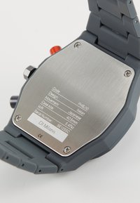 Orologio grigio con cinturino in gomma, retro in acciaio inossidabile con dettagli incisi, tra cui movimento, dimensioni della cassa e resistenza all'acqua.