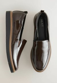 Scarpe slip-on in pelle patinata marrone con suola nera spessa, caratterizzate da pannelli elasticizzati laterali e una finitura liscia. Cuciture marroni accentuano il design.