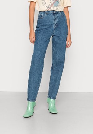 Jeans de ganga azuis de cintura alta com um corte reto, apresentando cinco bolsos e fecho de botão, usados com botas de tornozelo verdes menta brilhantes.