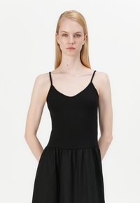 Μαύρο αμάνικο φόρεμα με V-λαιμόκοψη και στενή σιλουέτα, που φάρυνει σε μια πτυχωτή φούστα. Φτιαγμένο από λείο ύφασμα με ματ φινίρισμα.