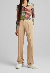 Farbige, leichte Button-Down-Bluse mit langen Ärmeln und beigen, gefalteten Hosen, kombiniert mit weißen Sneakern. Glatte Textur, zeitgemäße Passform.