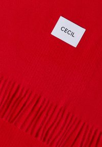 Écharpe en laine rouge avec bords frangés et une étiquette tissée blanche portant l'inscription "CECIL", cousue près d'une extrémité.