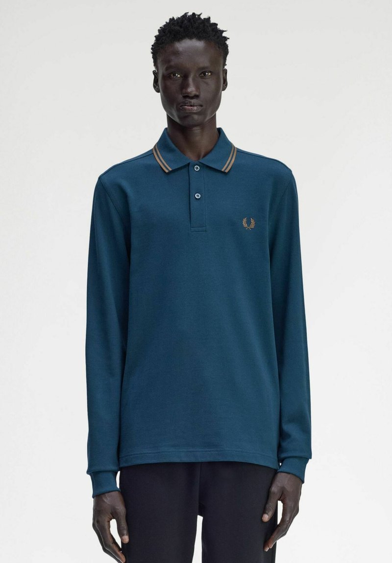 Polo a maniche lunghe in cotone di un profondo colore teal. Presenta un colletto a righe marroni, una patta con due bottoni e un logo ricamato sul petto.