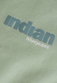 Tessuto di cotone verde con finitura testurizzata che presenta le parole "indian" in blu scuro e "bluejeans" in bianco, stampate centralmente.