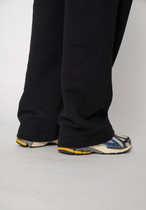 Pantaloni de trening negri, largi, cu tivuri elasticizate, asortați cu pantofi sport multicolori, prevăzuți cu talpă texturată și accente reflectorizante.