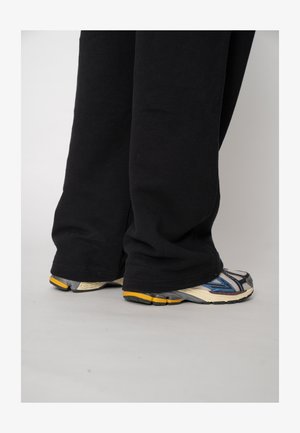 Pantaloni de trening negri, largi, cu tivuri elasticizate, asortați cu pantofi sport multicolori, prevăzuți cu talpă texturată și accente reflectorizante.