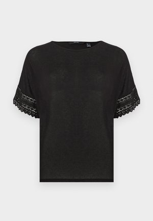 Musta lyhythihainen neulepaita pyöreällä kaula-aukolla ja pitsikoristeilla hihoissa, esitetty yksinkertaisella vaaleanharmaalla taustalla.