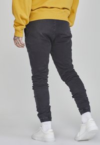 Schwarze, taillierte Jogginghosen mit elastischen Bündchen, aus Denim, kombiniert mit einem gelben Sweatshirt und weißen Sneakers mit strukturierten Akzenten.