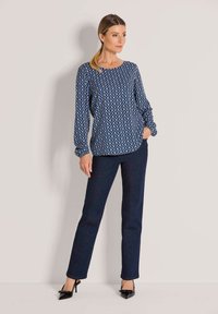 Navy patterned blouse with white zigzag design, long sleeves, and relaxed fit. Paired with dark blue straight-leg jeans and black heels.