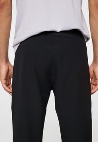 Czarne, dopasowane spodnie o gładkiej fakturze, z szerokim elastycznym pasem. Widok pokazuje tył, z minimalnymi detalami szwów.