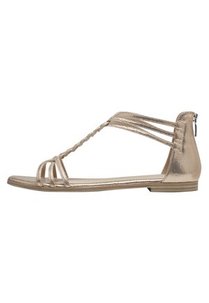 Flad gylden sandal med tynde flettede og glatte stropper, åben tå og lynlåslukning bagpå hælen.