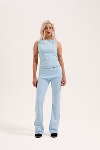 Ανοιχτό μπλε, εφαρμοστό αμάνικο τοπ με λογότυπο, σε συνδυασμό με ταιριαστά φαρδιά παντελόνια. Λείο ύφασμα με ελαφριά γυαλάδα. Μαύρα παπούτσια.