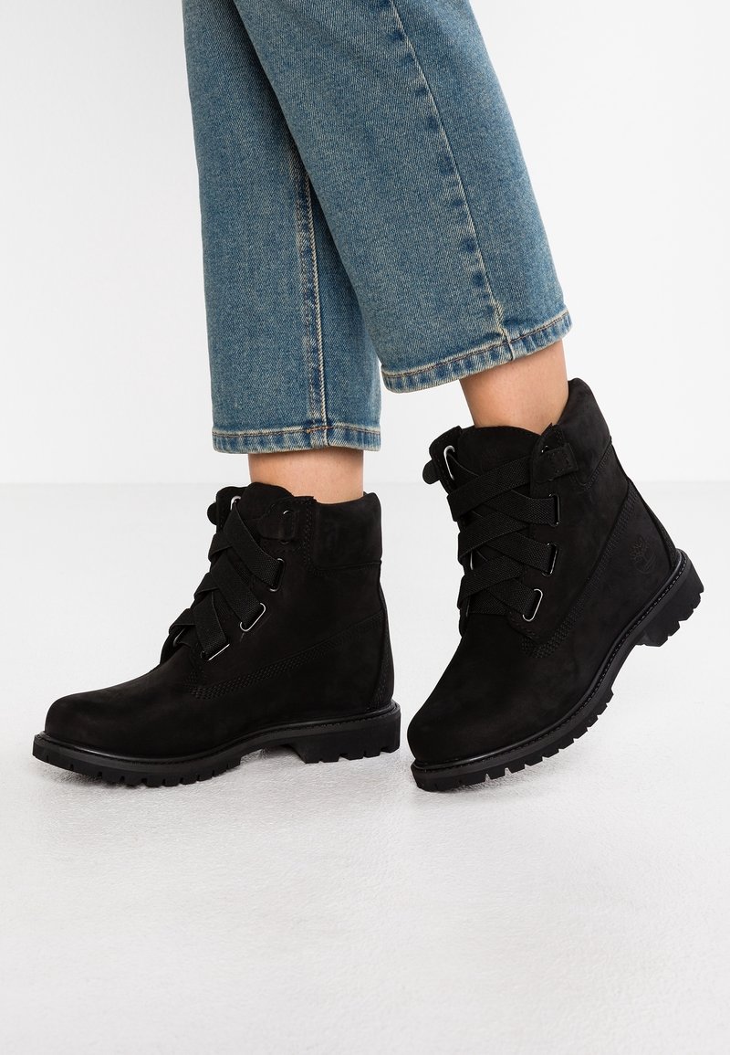 Black suede ankle boots with textured surface, featuring black laces, metal hardware, and rugged black rubber soles.