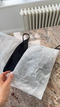 Schwarze Spitzen-Camisole, teilweise aus weißem Seidenpapier sichtbar, auf einer strukturierten Granitoberfläche platziert, mit einem Heizkörper im Hintergrund.