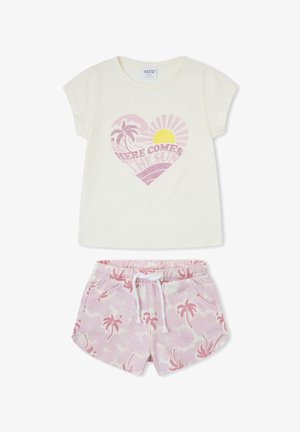 Camisa crema de manga corta con corazón rosa, gráfico de palmera y sol y texto "Here comes the sun", combinada con shorts rosa con estampado de palmeras.