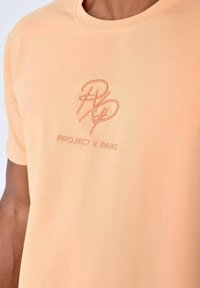 Camiseta de manga corta en color melocotón hecha de una tela suave, con un logo bordado en un tono ligeramente más oscuro justo debajo del escote.