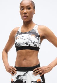 Fekete-fehér sportmelltartó absztrakt mintákkal, narancssárga díszítéssel. Puha anyag, racerback kialakítás és kontrasztos fekete szegély.