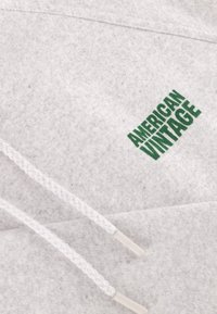 Sweat-shirt gris clair avec un cordon tissé blanc et un logo vert "AMERICAN VINTAGE" sur le devant. Texture douce avec un design décontracté.