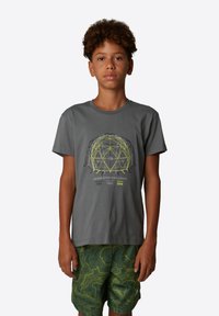 Camiseta de algodón gris con cuello redondo y mangas cortas, con un gráfico geométrico amarillo y texto. Combinada con pantalones cortos verdes de patrón ondulado.