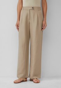 Beige hochtaillierte weite Hosen mit vorderen Falten, einem einzigen Knopfverschluss und einem glatten Stoffgefühl. Kombiniert mit tanfarbenen Sandalen.