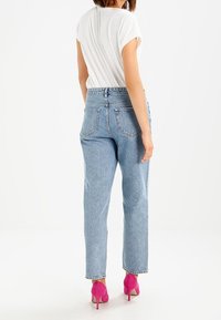 Vaqueros de tiro alto de color azul claro con un ajuste relajado y textura desgastada, combinados con una camiseta blanca y zapatos de tacón rosa.