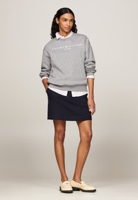 Felpa grigia con logo bianco, indossata sopra una maglietta a righe rosa. Una gonna blu e mocassini crema completano l'outfit.