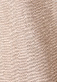 Gros plan sur un tissu beige et marron clair tissé avec un subtil motif chevron et une surface texturée.
