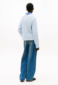 Maglione lavorato a maglia azzurro chiaro con un motivo testurizzato, abbinato a jeans in denim blu a gamba larga. L'insieme è completato da calzature nere.