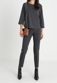 Top grigio a quadri e pantaloni fitted abbinati; tessuto testurizzato con un motivo sottile. Borsa a tracolla in stampa serpente piccola; stivali neri con tacco a punta.