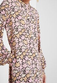 Blommig långärmad skjorta i rosa, creme och svart. Har knäppning framtill, rundad krage och ett detaljerat lövmönster med texturerade inslag.