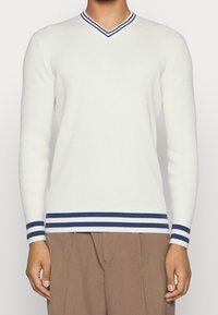 V-hals sweater i creme med navystribet ribkant ved halsudskæring og ærmekanter. Fremstillet af blødt strikkemateriale, figursyet silhuet, lange ærmer.