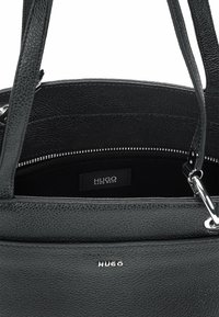 Borsa a tracolla in pelle nera con finitura testurizzata, dotata di accessori in argento, un compartimento con cerniera e un'etichetta del marchio riconoscibile all'interno.