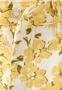 Gros plan sur un tissu jaune à motif floral sur un vêtement avec un bouton en métal et une boucle de ceinture cousue.
