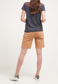 Vue arrière d'une personne portant un t-shirt gris avec un design en dentelle sur les épaules, un short beige et des baskets blanches avec un accent en imprimé léopard.