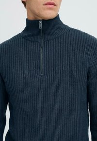 Navy zip-neck sweater made of textured knit material, featuring a high collar and a short zipper at the front.