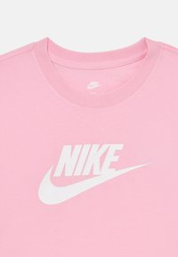 Rožinė medvilninė marškinė su dideliu baltu Nike logotipu ir swoosh dizainu priekyje. Apvalus kaklo iškirpimas su lygiu paviršiumi.