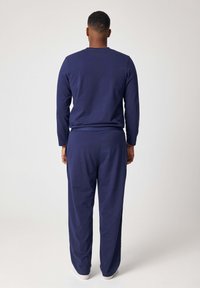 Top a maniche lunghe blu navy e pantaloni abbinati in tessuto morbido, caratterizzati da una vestibilità rilassata e da una cintura elastica, visti da dietro.