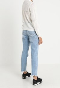 Maglione chunky bianco a maglia aperta, jeans dritti azzurri con orlo sfrangiato e scarpe da ginnastica nere.