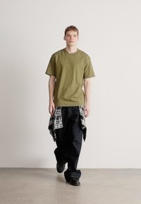 Olivne zelena kratka majica s kratkimi rokavi, kombinirana z velikimi temno modrimi kavbojkami in črno-belo karo srajco, vezano okoli pasu. Črni čevlji.