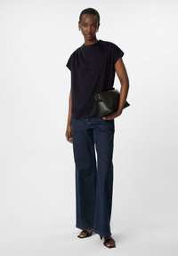 Marineblaues Kurzarmoberteil, kombiniert mit dunkelblauen, weit geschnittenen Jeans und schwarzen, hohen Sandalen. Schwarze Clutch-Tasche mit faltigem Design.