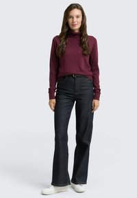 Maglione a collo alto color bordeaux abbinato a jeans svasati in denim scuro a vita alta. Sneakers bianche e una semplice cintura nera completano l'outfit.