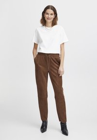 Brown suede jogger pants with a drawstring waist and side pockets, paired with a white short-sleeve t-shirt and black ankle boots.
