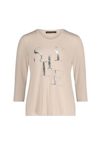 Beżowa koszula z długim rękawem z metalicznym srebrnym napisem "STYLE" ozdobionym ćwiekami. Gładka tekstura i luźny fason.