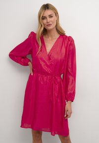 Rochie în fuchsia, realizată dintr-un material u�șor, cu mâneci lungi puff, decolteu în V și un detaliu cu talie legată. Textură netedă.