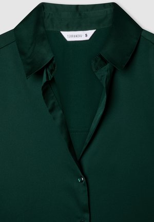 Ciemnozielona satynowa bluzka z klasycznym kołnierzykiem, zapinana na guziki, o gładkiej fakturze. Metka zaznacza rozmiar S od Terranova.